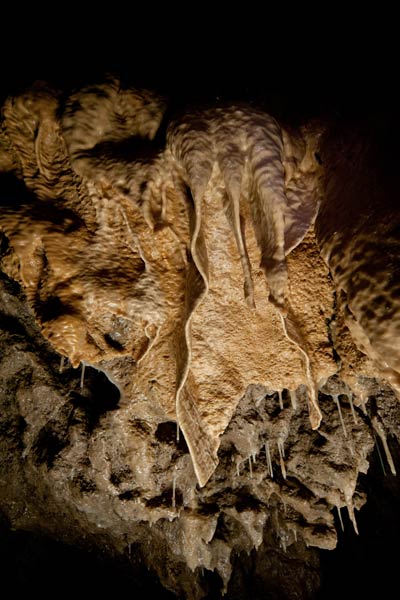 Calcite drapery speleothems inside Rat's Nest Cave, Canmore Alberta — banded cave formations showing thousands of years of mineral deposits in the Canadian Rockies