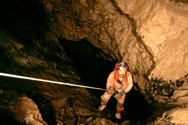 Caver rappelling into vertical shaft inside Rat's Nest Cave, Canmore Alberta — rope descent during exploration of Canadian Rockies cave system near Banff